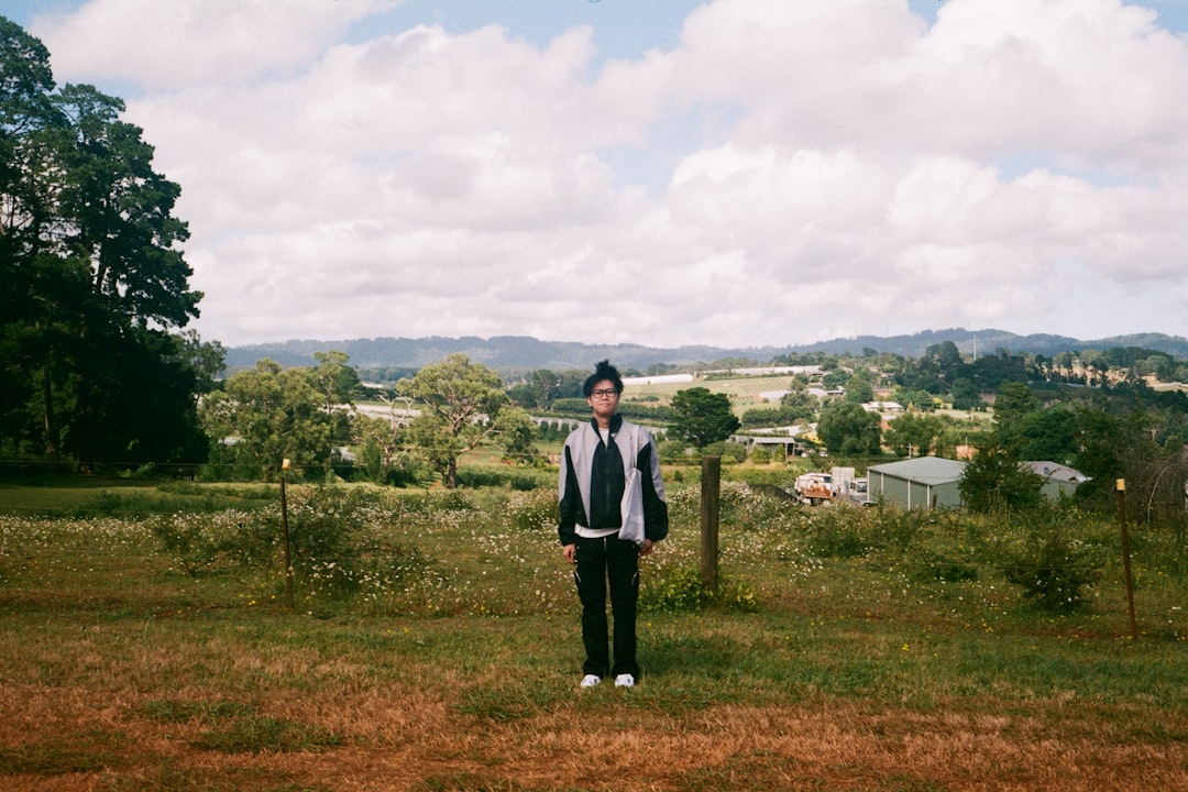 Man standing in a rural field with trees and clouds.
